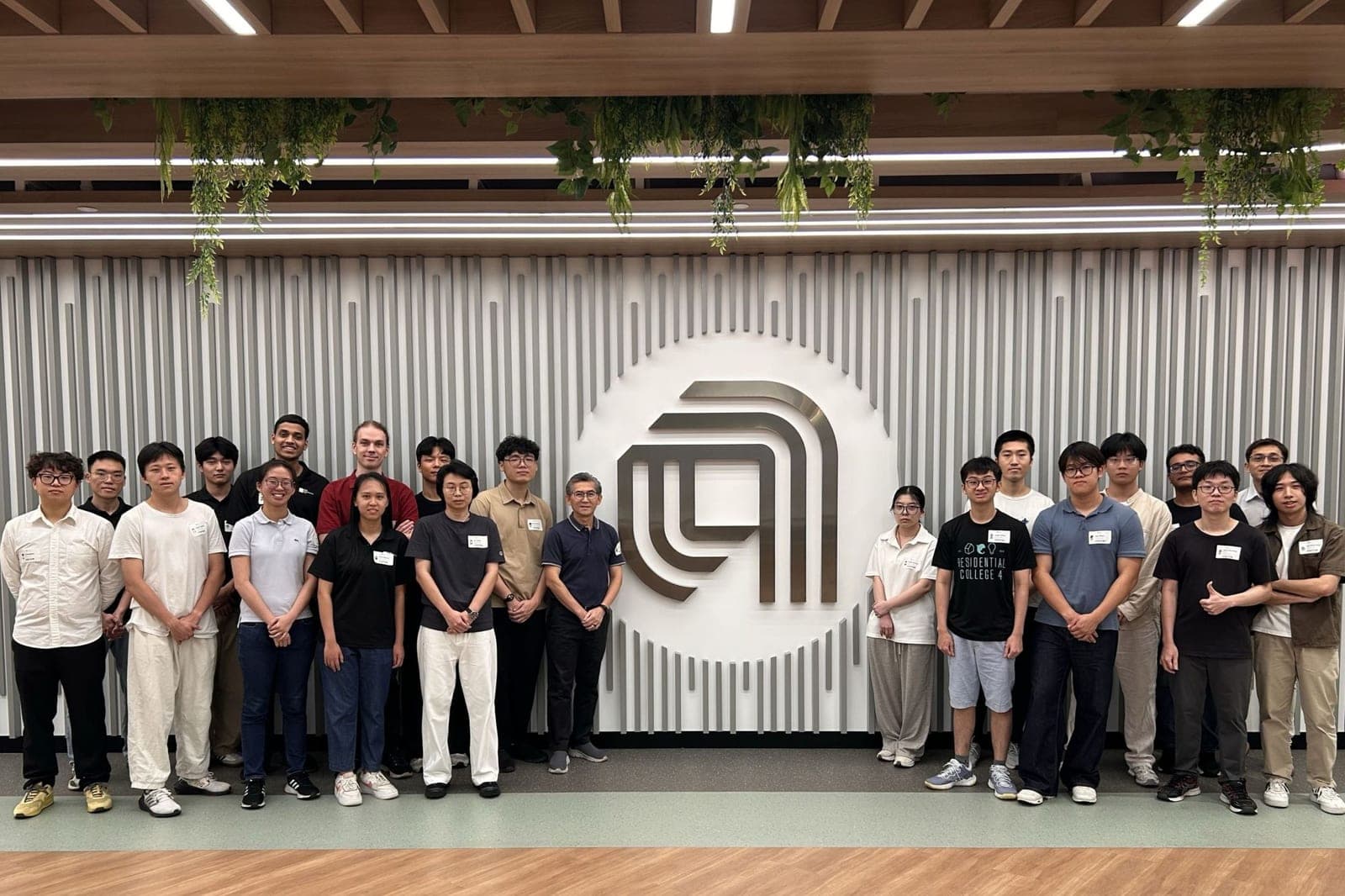 The visiting group standing in two rows either side of the Applied Materials emblem on a slatted feature wall at the Tampines campus
