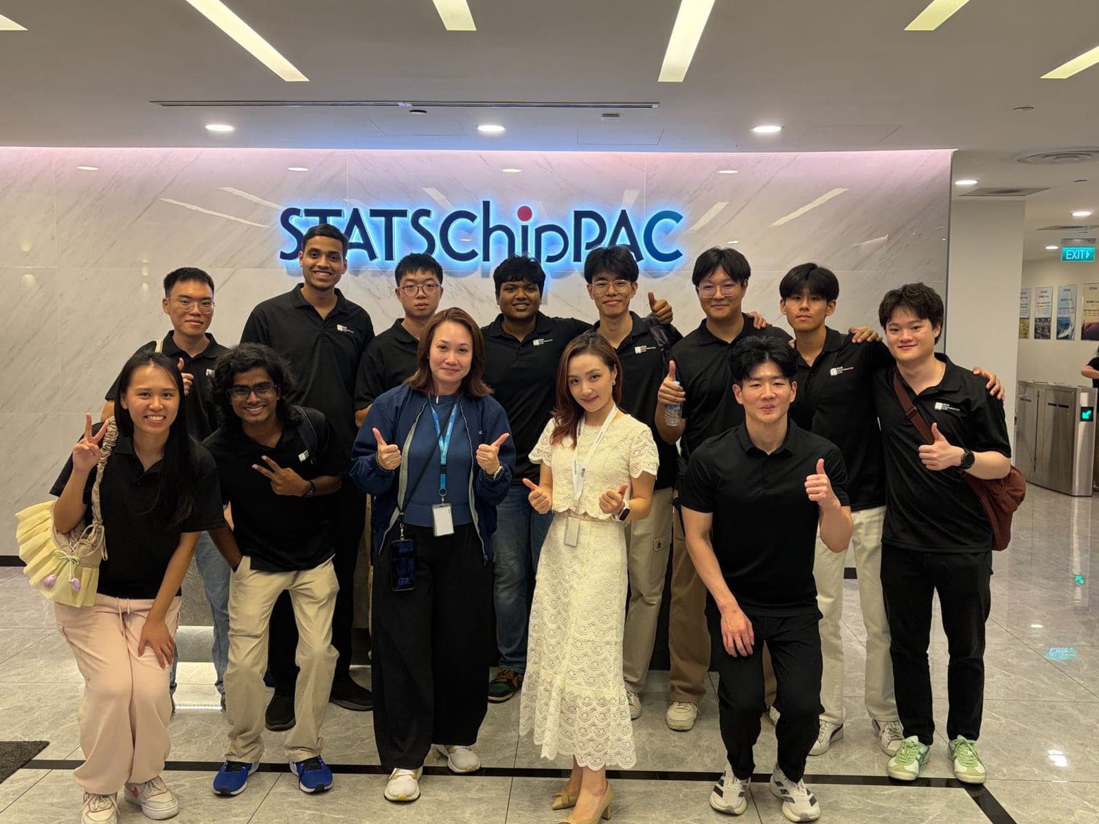 The visiting group with two STATS ChipPAC staff, giving thumbs up in front of the illuminated STATSChipPAC sign in the lobby